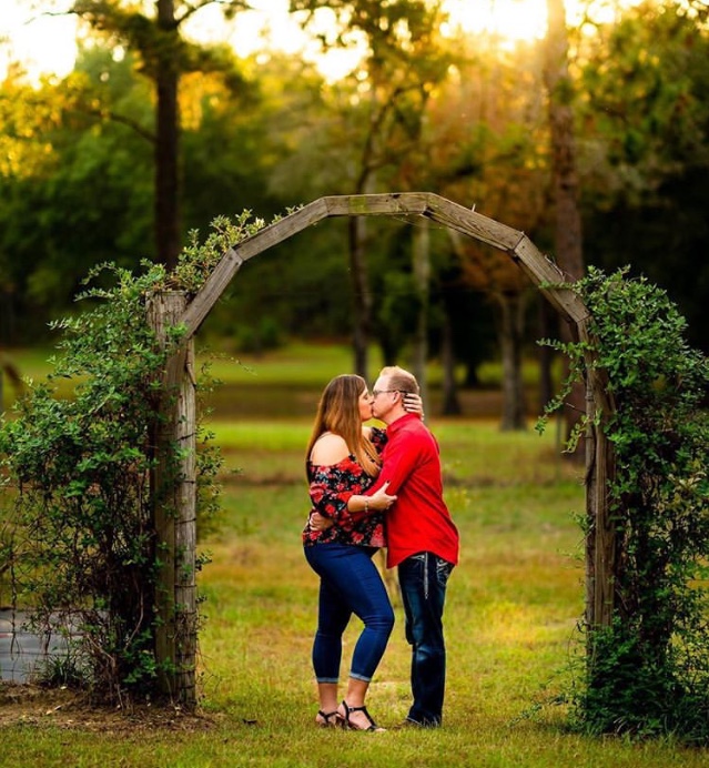 couple dressed in red sharing a cupids kiss under an arbor