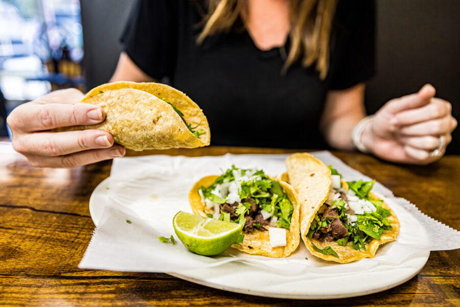lady holding a La Joya taco over a plate of tongue tacos smothered in cilantro and onions.