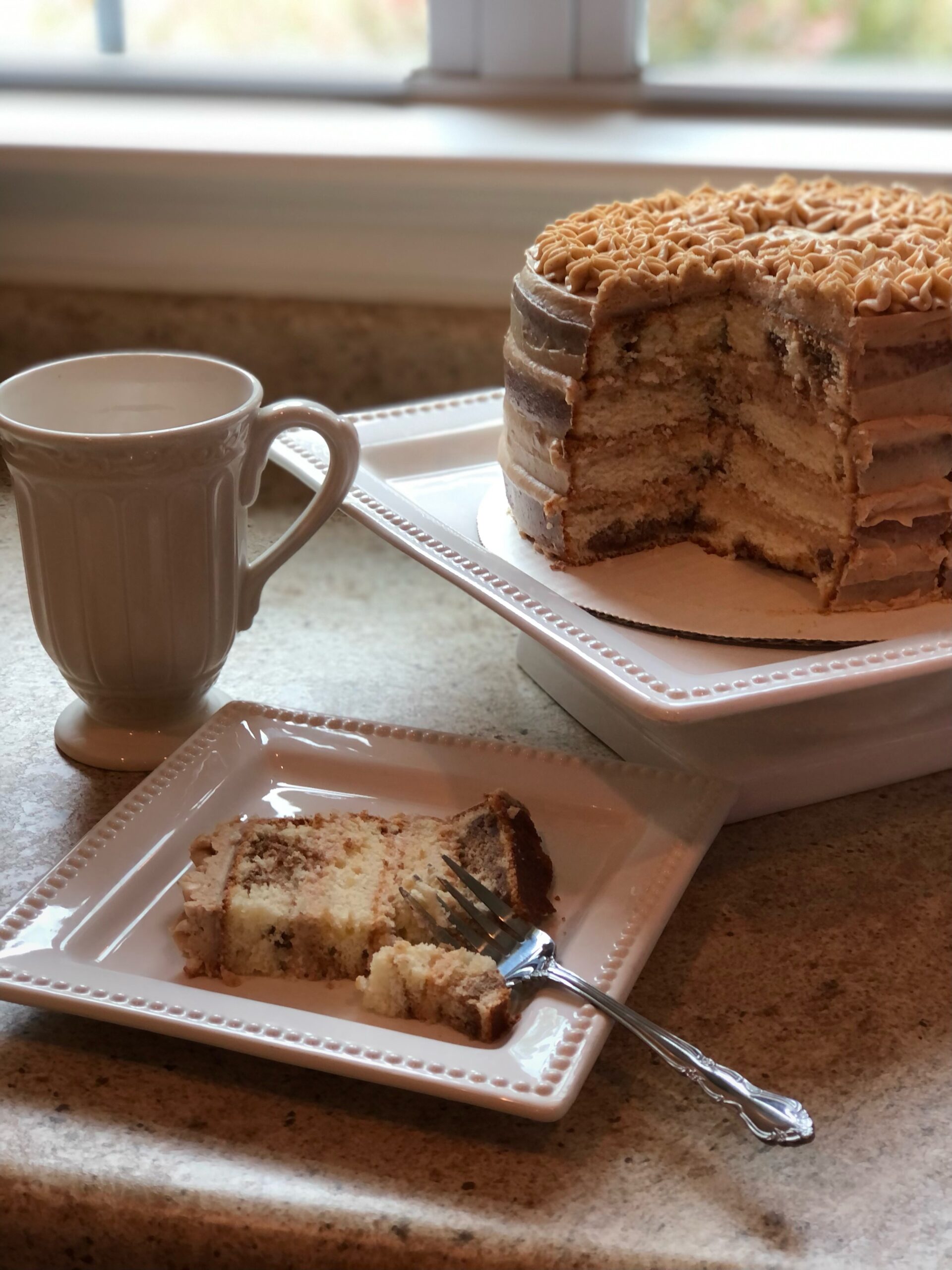 a slice of snickerdoodle cake in front of the cake and a cup of tea