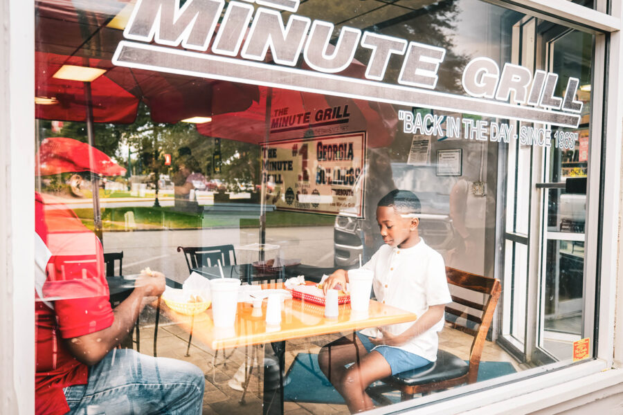 Man and child seen from the sidewalk, through the window of the Minute Grill.