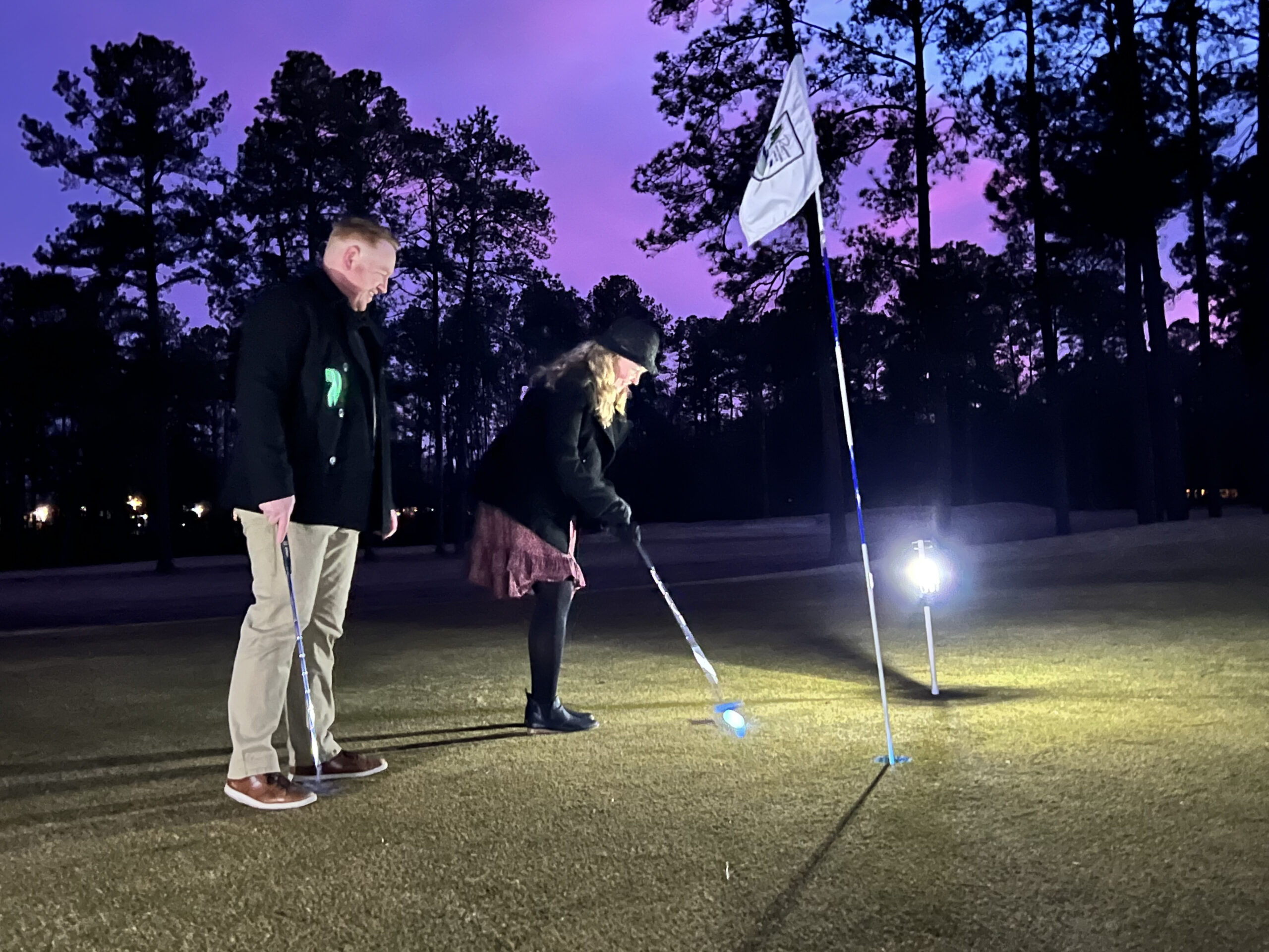 A couple putting on greens lit by lanterns during the Hearts & Clubs sweetheart putt-putt date