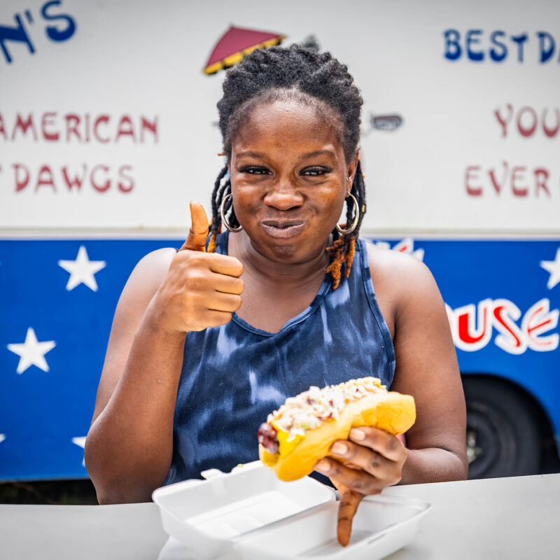 Woman enjoying a Don's Dog sitting at a picnic table outside the food truck.