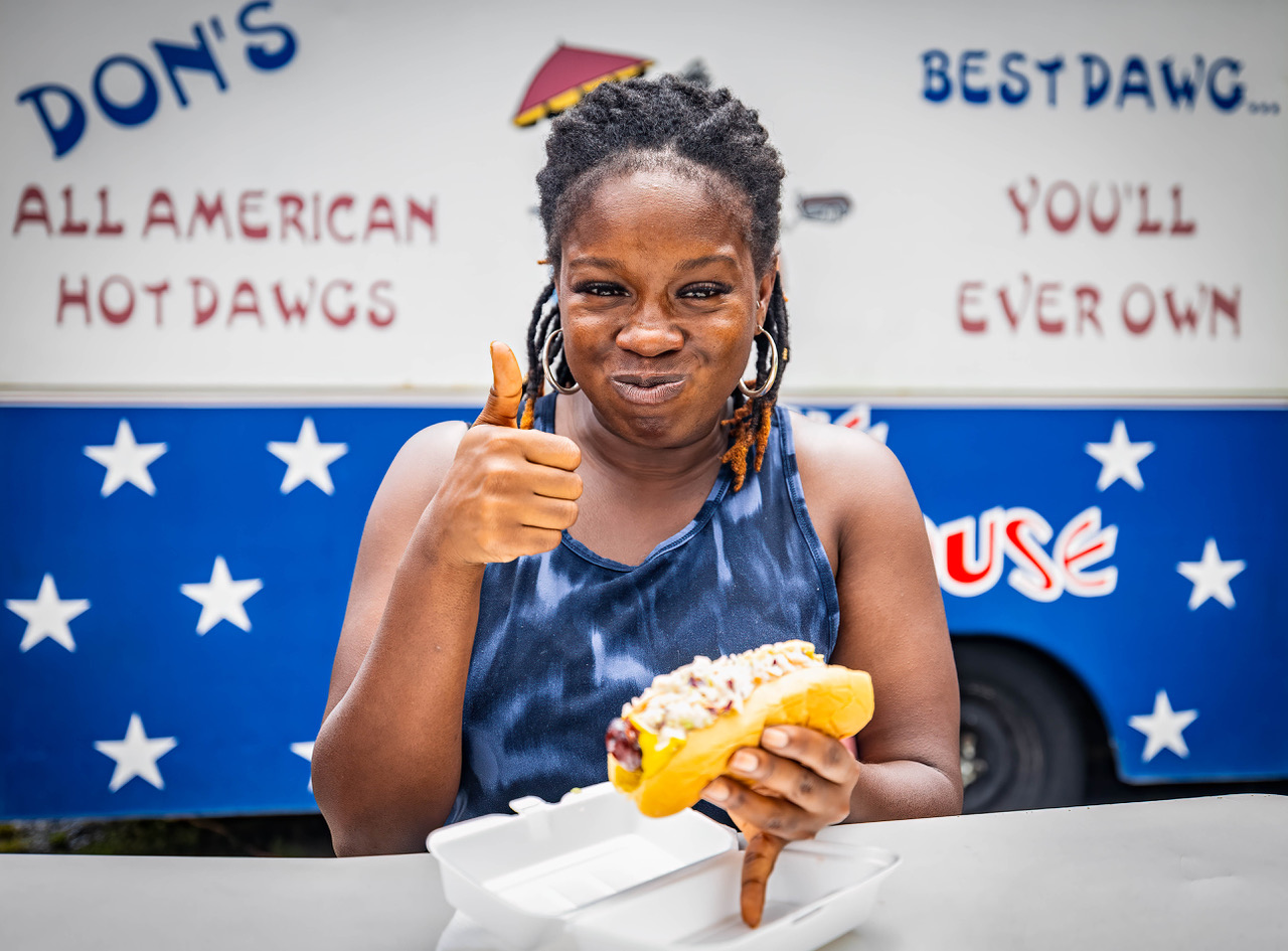 Woman enjoying a Don's Dog sitting at a picnic table outside the food truck.