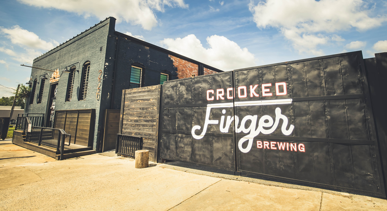 Exterior view of Crooked Finger Brewing showing the huge logo painted on the privacy fence butting against the sidewalk.