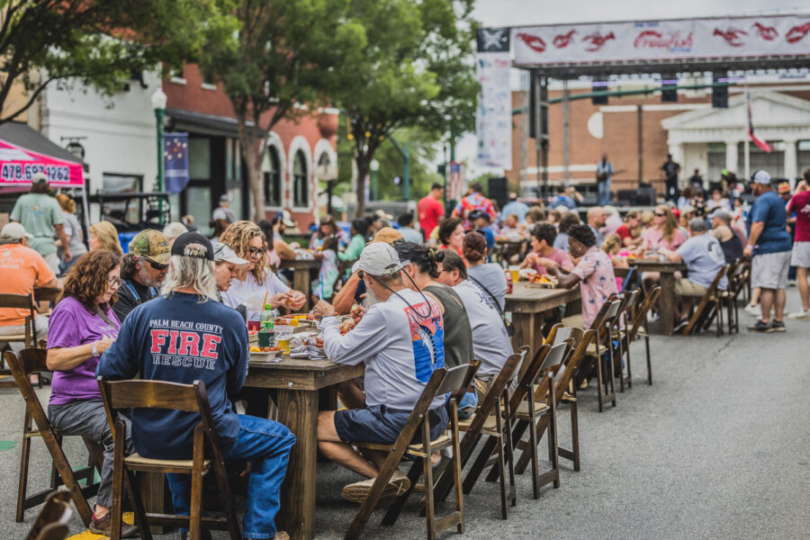 People sitting at tables lined up in the street in front of the stage at the Bon Temps Crawfish Festival.