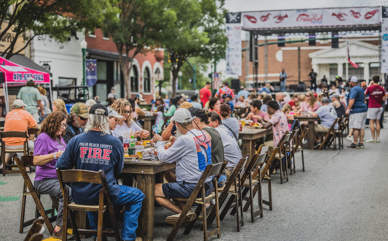 People sitting at tables lined up in the street in front of the stage at the Bon Temps Crawfish Festival.