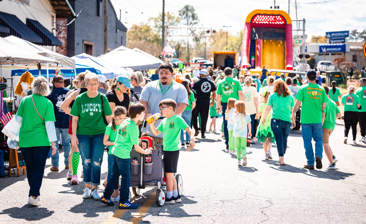 A street filled with people wearing green strolling past vendors at the Arts & Craft Festival.