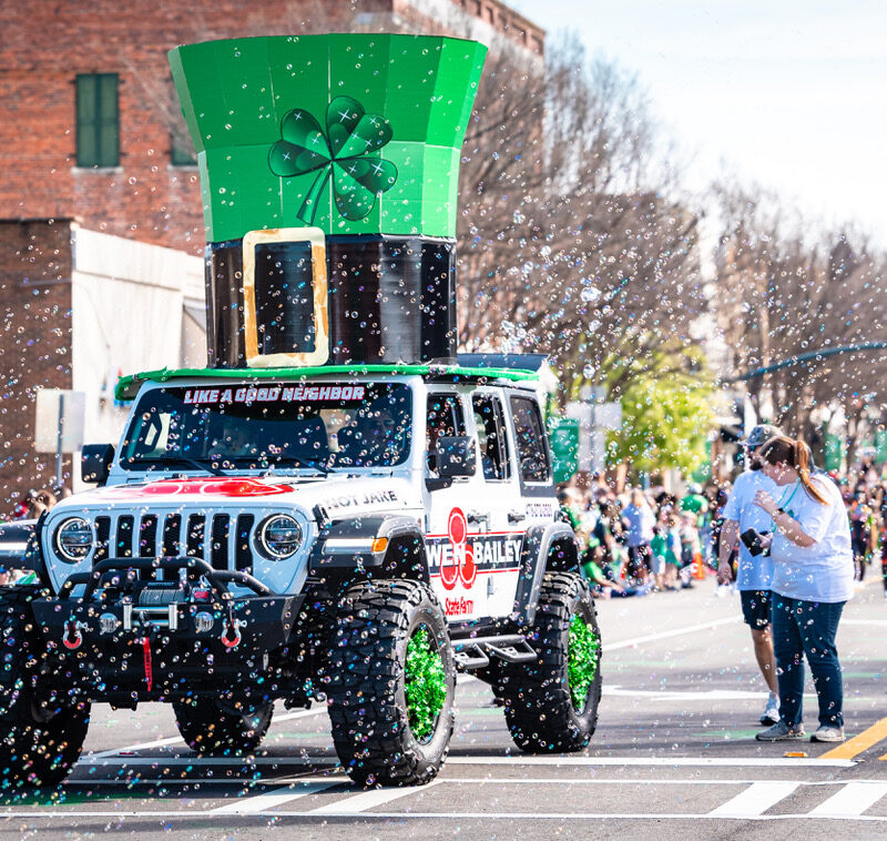 A giant green top hat adorned with a shamrock on top of a white Jeep in the St. Patrick's parade shows that the St. Patrick's Festival is super fun!