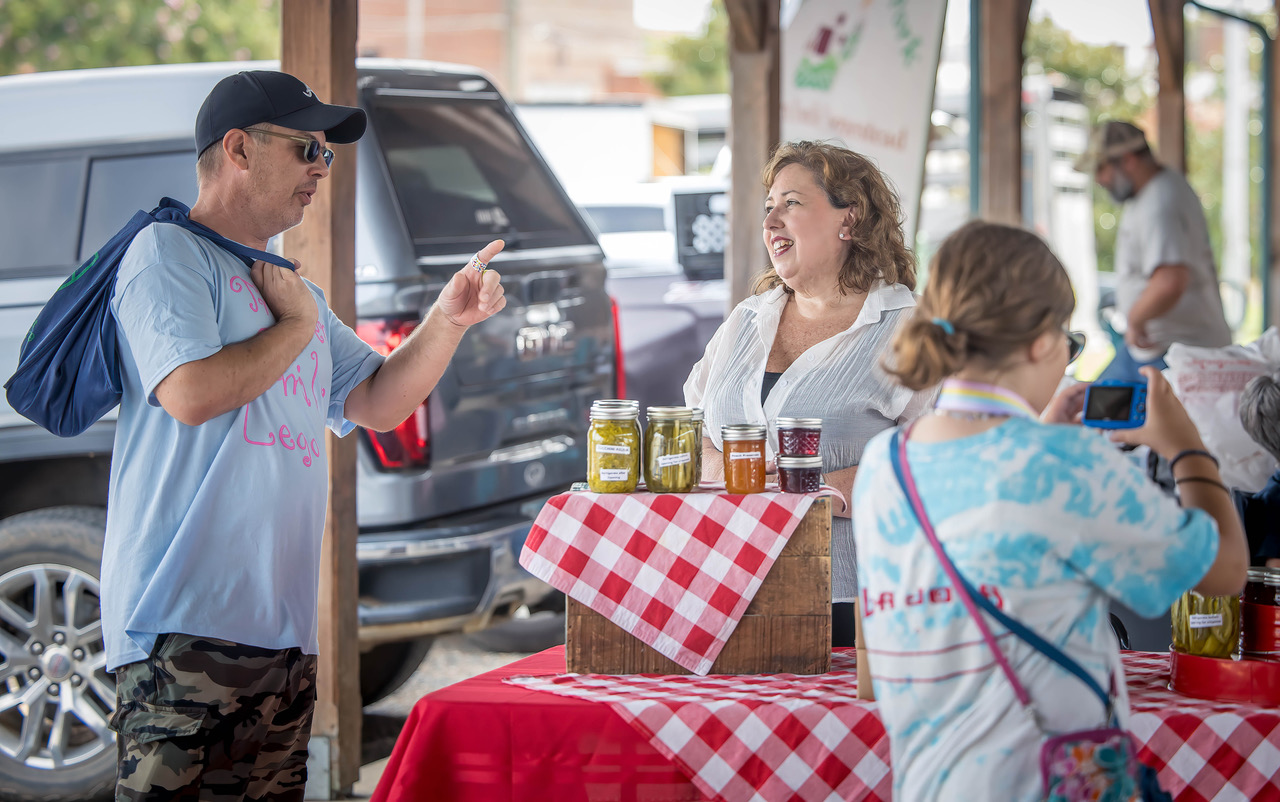 Elaine Avery chatting with a custom at her red checkered baked goods table.