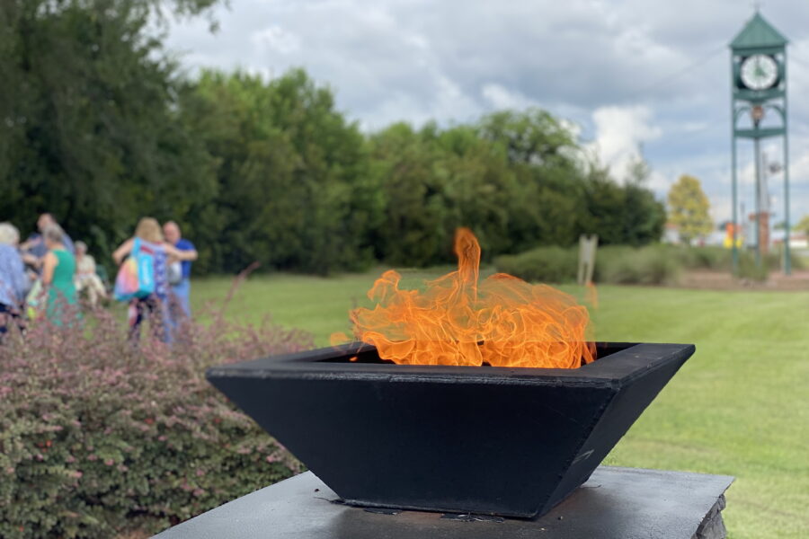 Everlasting flame in foreground and people attending Bells Of Freedom and Dublin's bell that is rung during the event in the background, all in Railroad Park.