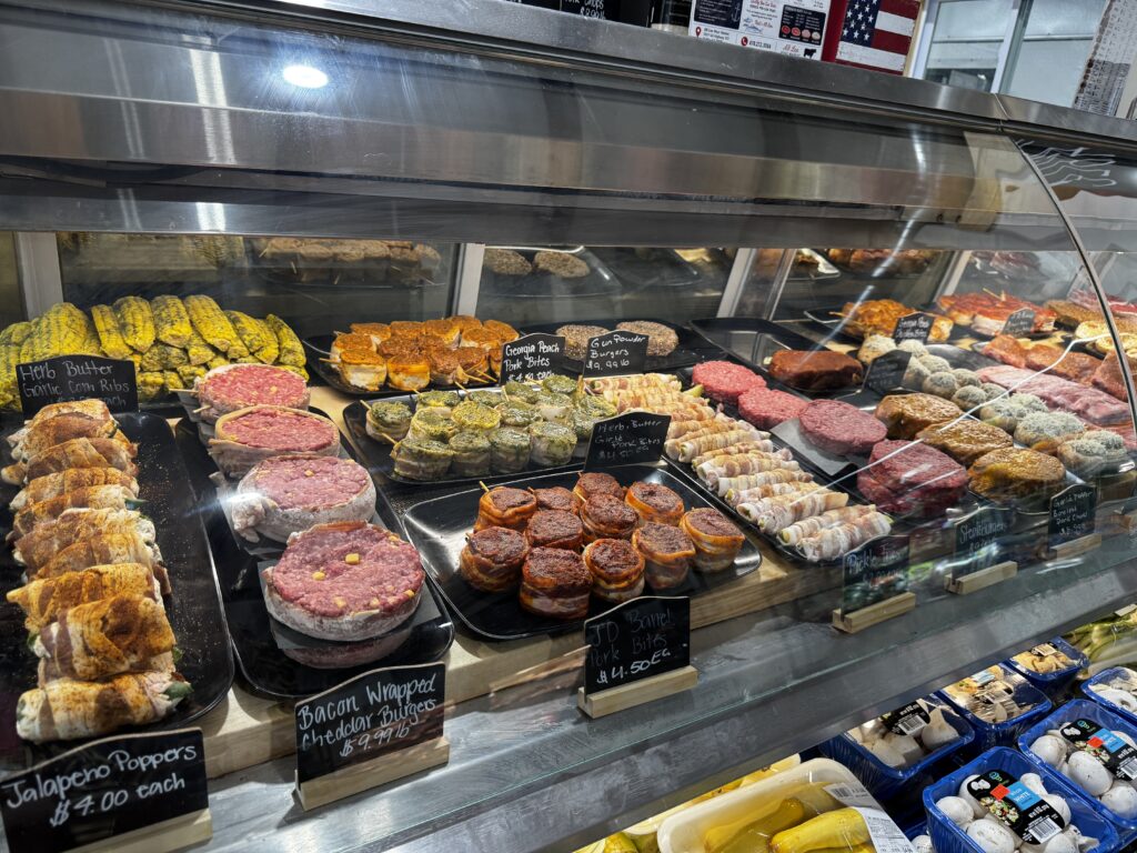 View of A. B. Lee's Marinade Bar full of differently marinated pork and beef cuts as well as corn and bacon wrapped veggies.
