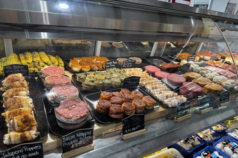 View of A. B. Lee's Marinade Bar full of differently marinated pork and beef cuts as well as corn and bacon wrapped veggies.