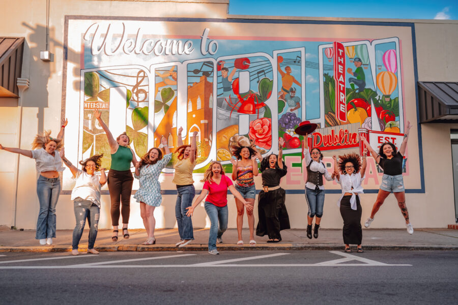 Ladies enthusiastically jumping in front of a colorful Dublin GA mural.