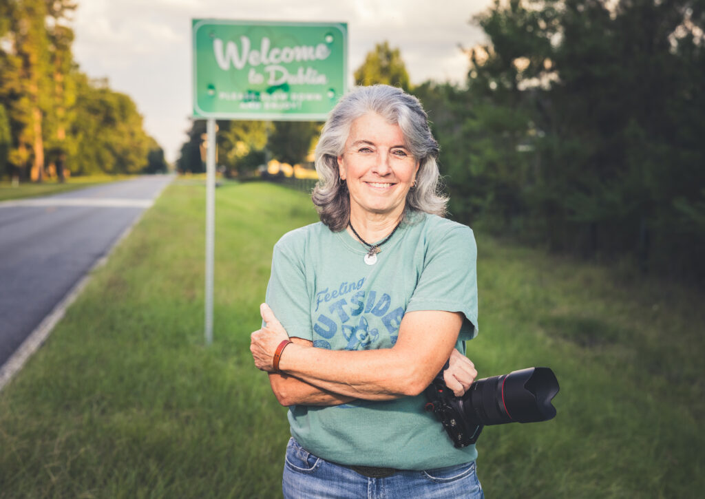 Photo of Kellie Oliver holding a camera, standing in front of a Welcome To Dublin road sign.