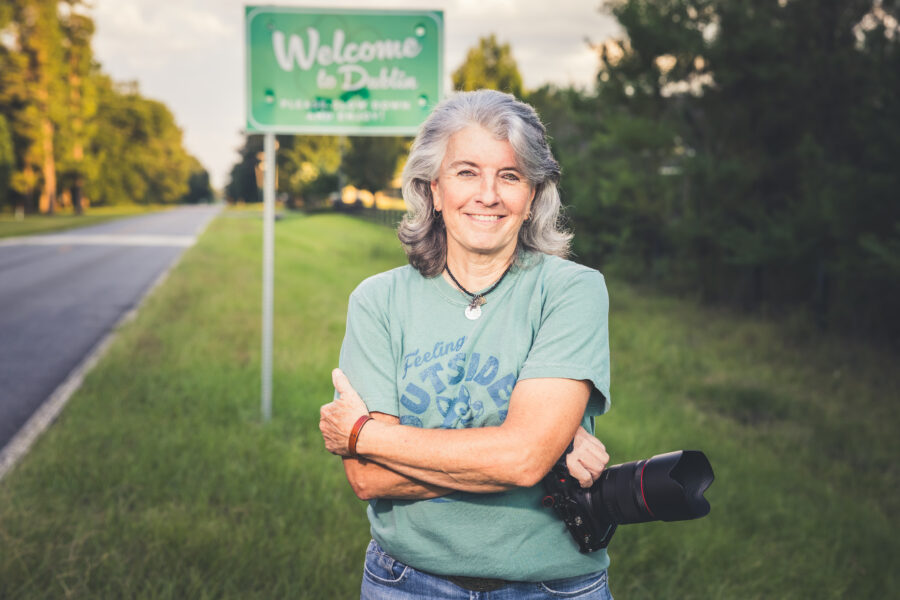 Photo of Kellie Oliver holding a camera, standing in front of a Welcome To Dublin road sign.