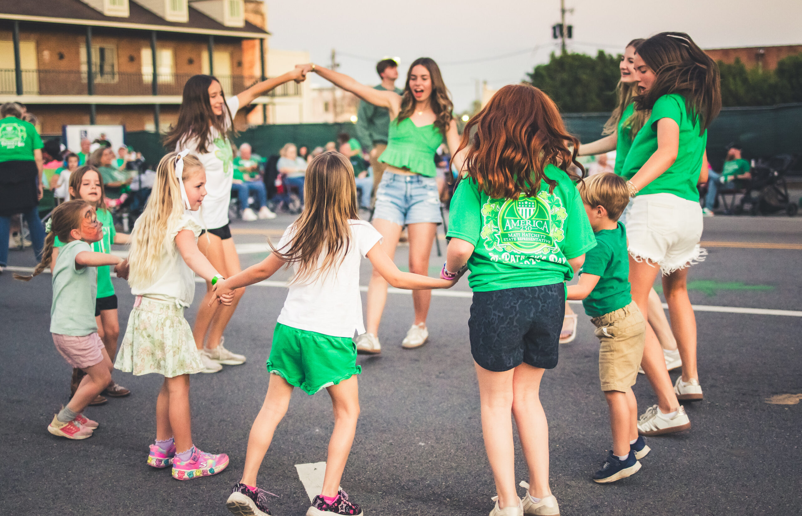 Young children dressed in green dancing in a circle in the street during St. Patrick's Music & Munchies.