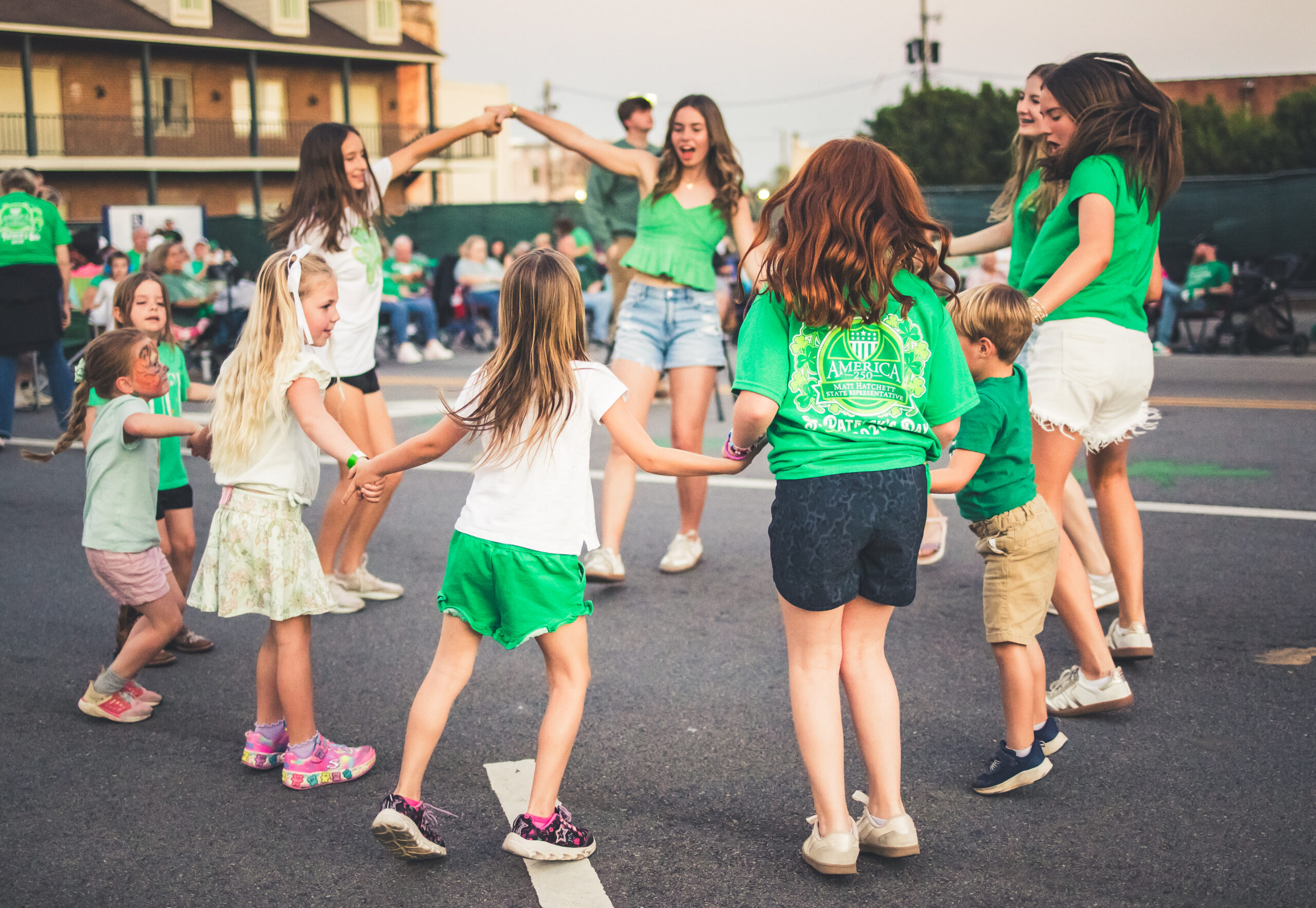 Young children dressed in green dancing in a circle in the street during St. Patrick's Music & Munchies.