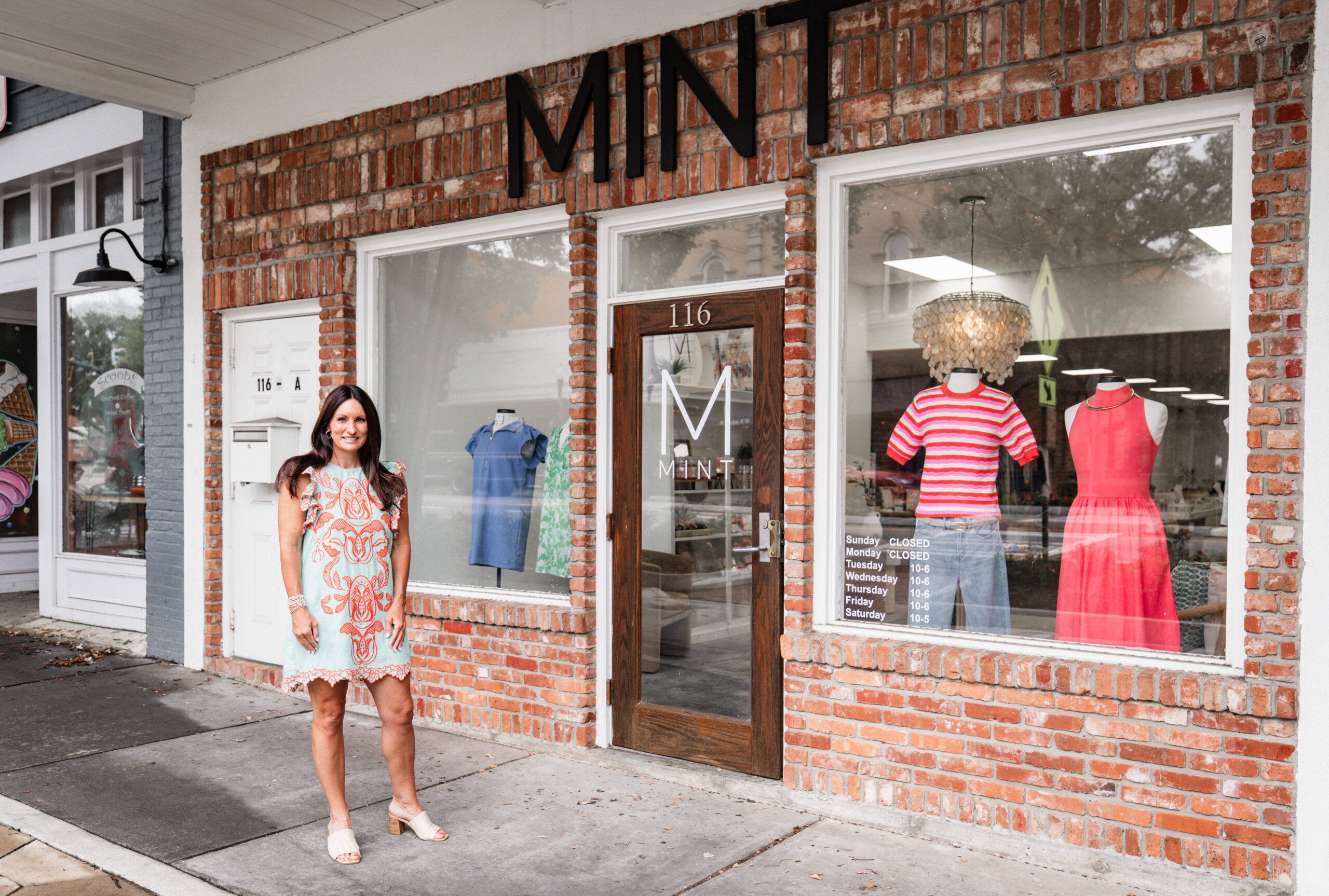 Owner Laura Wilson standing outside of Mint Boutique's bright window scenes.