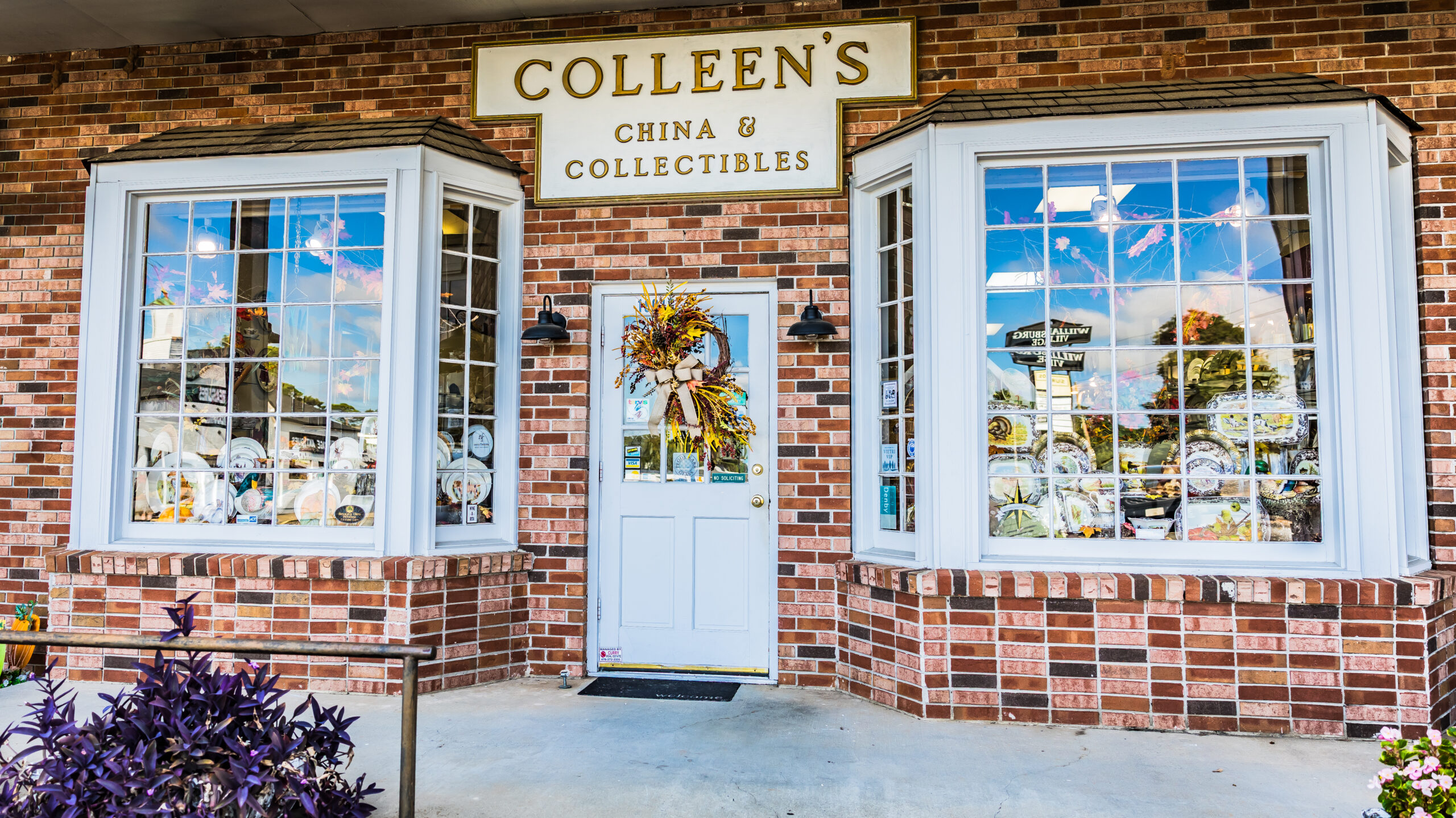 The exterior of Colleen's China showcasing the tableware display in two windowns flanking the door adorned with a colorful wreath.