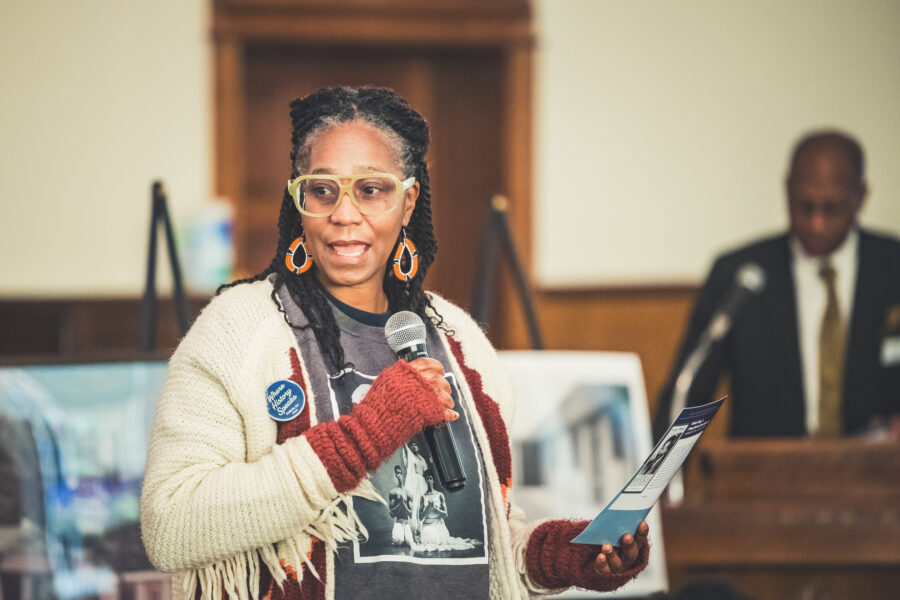 Woman speaks into a microphone, holding a card with her lines during One Day: Dublin's Civil Rights Experience